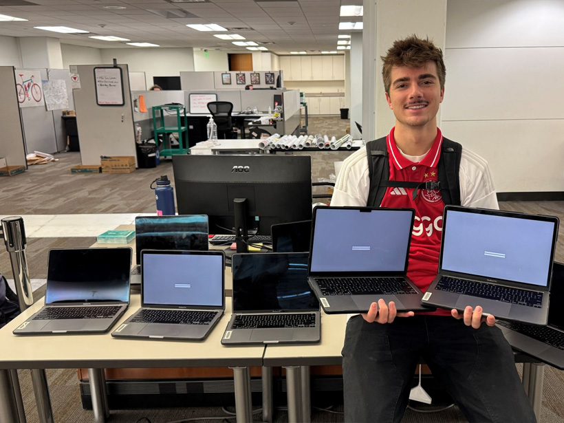 ASUU member Joseph sits near the knowledge commons desk surrounded by open laptops.