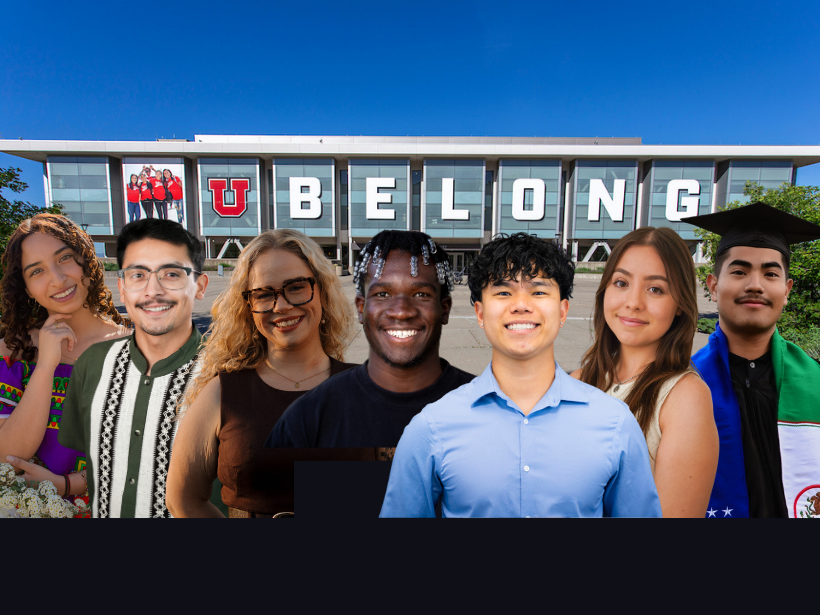 A diverse group of seven smiling individuals stand in front of a modern building with large letters spelling “U BELONG,
