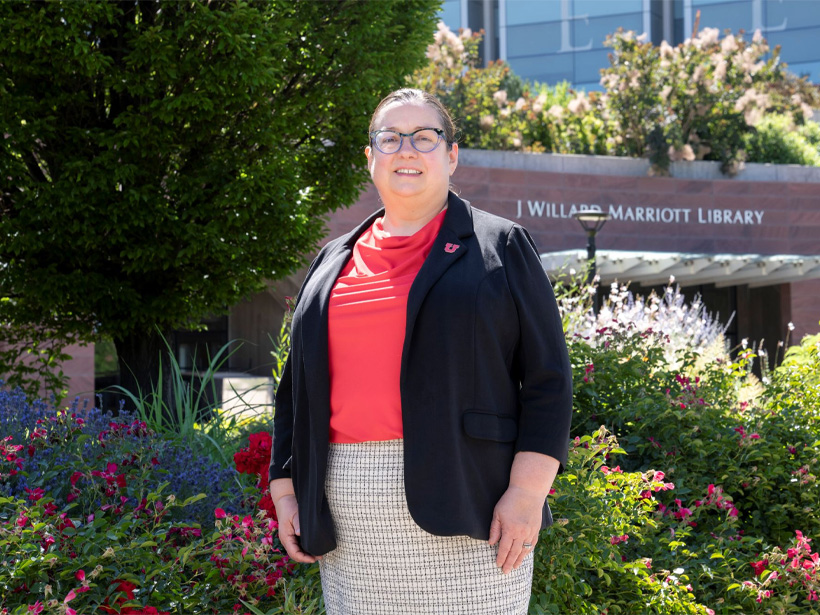 Dean Sarah Shreeves standing in front of the garden at the west entrance of the library. The day is very sunny and the flowers are all blooming.