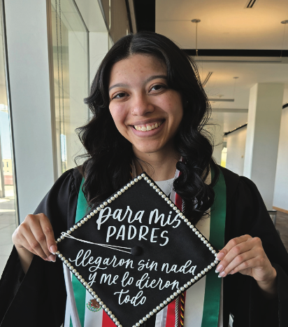 Keisha Jimenez in a graduation gown, holding her graduation cap that says Para Mis Padres, for my parents