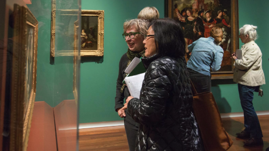 adults looking at art in the UMFA museum. One of the patrons glasses match the green walls.