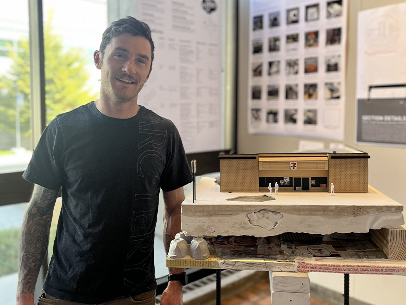 White man with a black shirt next to a small concrete architecture display